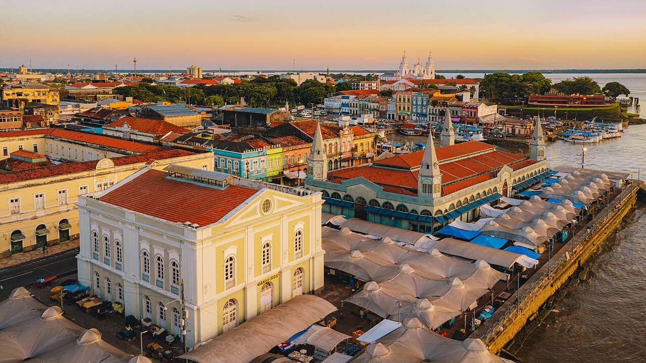 Vista aérea do centro histórico de Belém ao fim da tarde, com o Mercado de Ferro do Ver-o-Peso, casarões coloridos e a Baía do Guajará